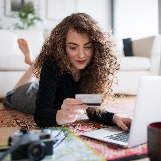young-woman-looks-at-credit-card-near-laptop
